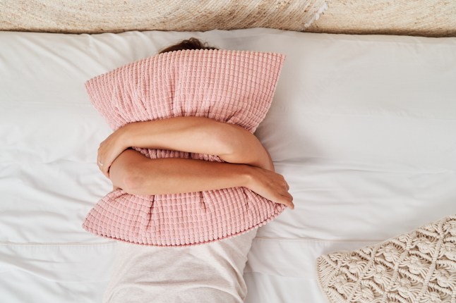 Top view of a beautiful young woman lying in bed covering her face with a pillow.