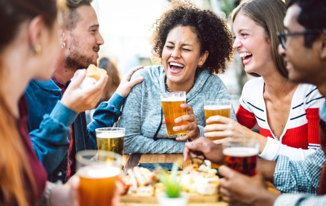 Multiracial friends drinking beer at brewery pub garden - Genuine friendship life style concept with guys and girls enjoying happy hour food together at open air bar dehor - Warm vivid filter