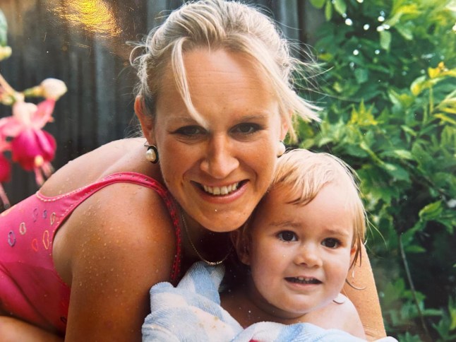 Amelia Wrighton with mum Cindy. They are in a garden setting. Cindy has wrapped Amelia in a towel. Both are smiling.